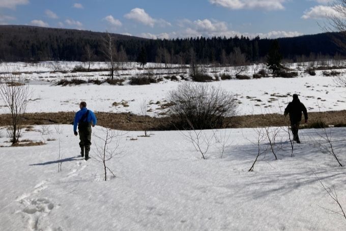 Zwei Männer laufen durch eine teilweise mit Schnee bedeckte Landschaft